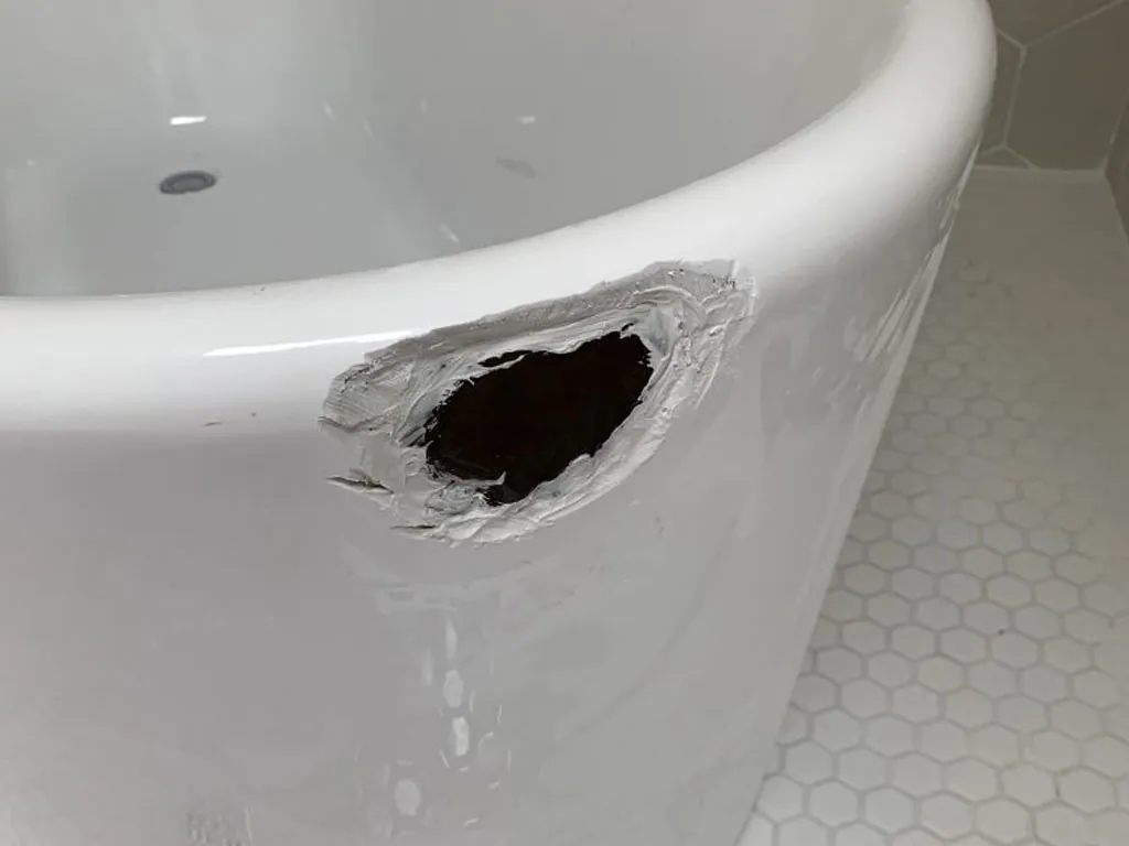Hole punched through the side of a new white freestanding tub, before