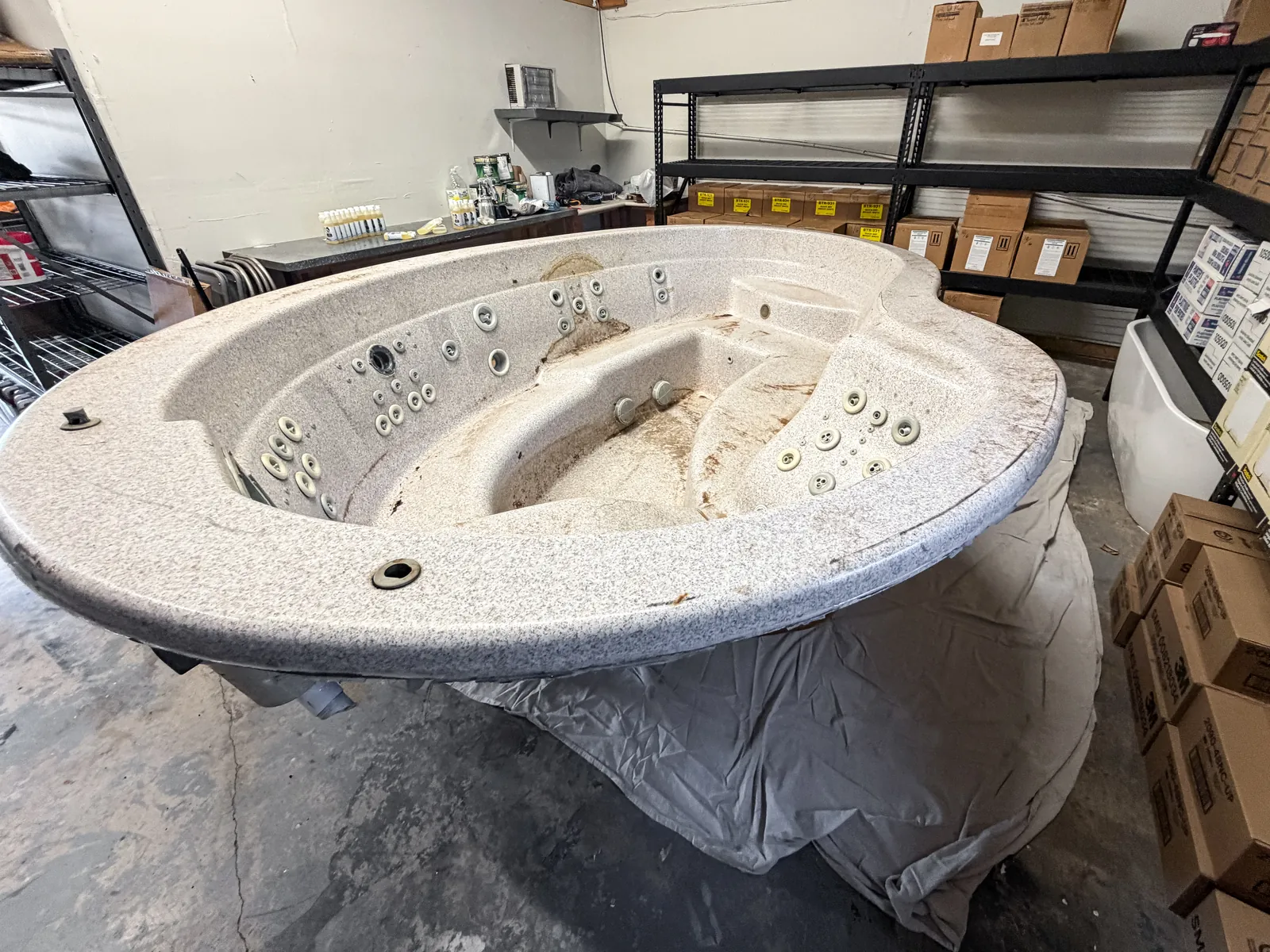 Full-size spa shell in the shop with a worn finish and jets still in, before